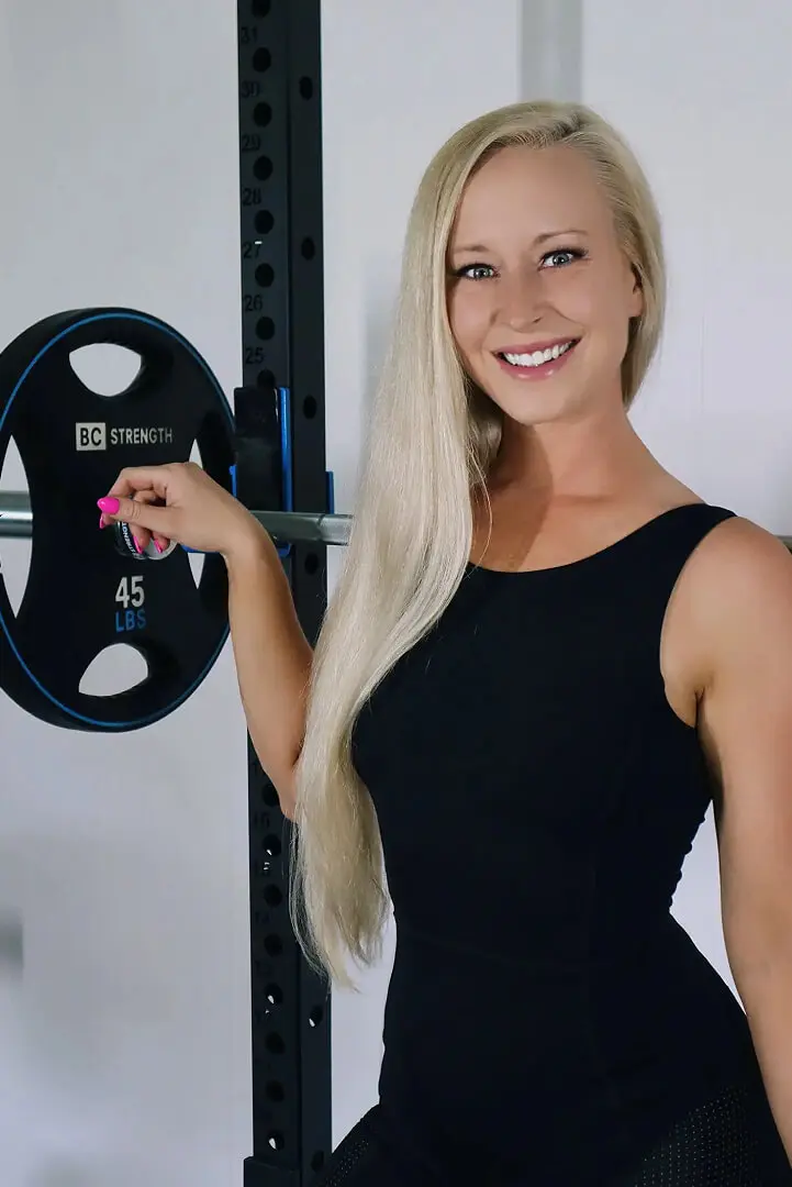 A woman holding onto a barbell in front of a wall.